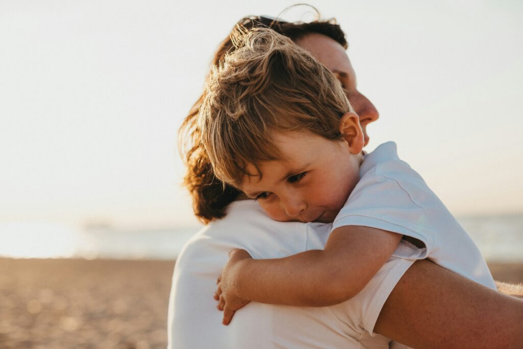 Child with autism embraced by a parent on the beach at sunset, symbolizing comfort, connection, and family support — Ready Set Connect Autism therapy and care.